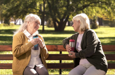 Two Old Ladies Drinking Hot Tea From Travel Mugs, Sitting On Ben