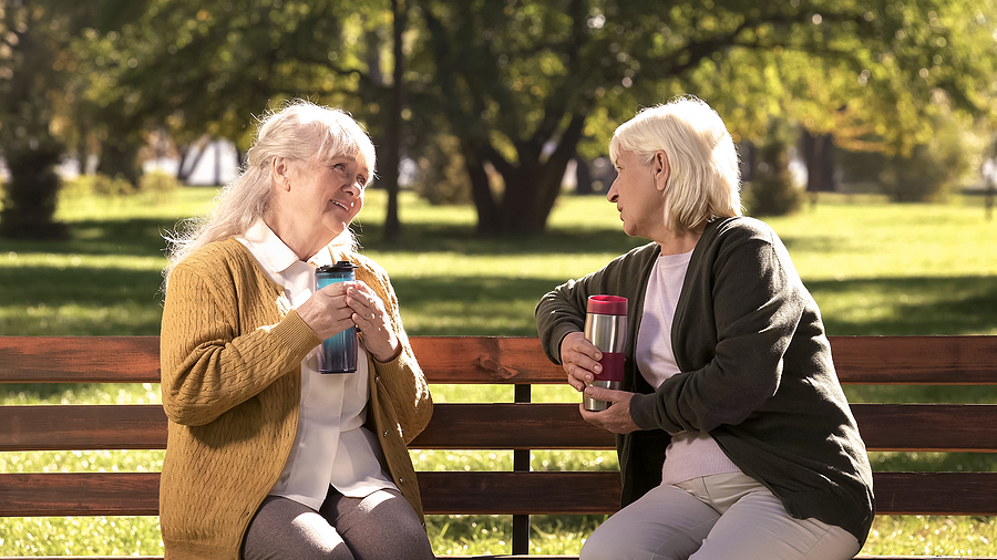 Two Old Ladies Drinking Hot Tea From Travel Mugs, Sitting On Ben